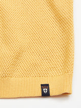 Close-up of Blue de Gênes yellow Filo Knit Polo - Yellow Grain, made from 100% cotton. The fabric features a honeycomb pattern and a small black tag with a white shield emblem topped by an orange design.