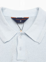 Close-up of the Blue de Gênes Filo Knit Polo - Blue Water, showcasing a retro repeat stitch pattern, three-button placket, and crafted from 100% cotton. The collar tag displays the brand name on a dark blue background.