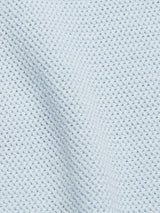 The Filo Knit Polo - Blue Water by Blue de Gênes features a textured light blue cotton fabric with a waffle weave pattern, reminiscent of a retro stitch. Its slightly raised grid-like design and soft sheen add depth and dimension.