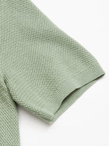 Close-up of the Blue de Gênes Filo Knit Polo - Green Bay, featuring a light green retro waffle pattern. The sleeve edge shows ribbed detailing at the hem. Crafted from 100% cotton, the fabric looks soft and comfortable.