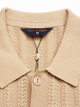 Close-up of a Compra Open Polo Knit shirt in khaki by Blue de Gênes, made from organic cotton, with a buttoned collar. It features an embroidered Blue de Gênes label above a shield logo and has a gold cross pendant on a green cord threaded through the top buttonhole.