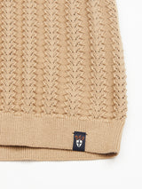 Zoom in on a khaki knit sweater with a zigzag design, made from organic cotton. The hem features a small black tag displaying BDG and a white cross symbol. The background is white. Product: Compra Open Polo Knit by Blue de Gênes.