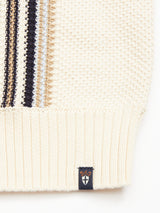 Close-up of the Cappa Stripe Cardigan - Whitecap by Blue de Gênes. Crafted from soft cotton, it features a ribbed hem and stylish beige, black, and blue stripes on the left side with a small black label emblazoned with a crown and shield emblem sewn on the hem.