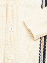 A close-up of the Blue de Gênes Cappa Stripe Cardigan - Whitecap in cream-colored cotton yarn, highlighting its textured patterns, ribbed sleeve cuffs, button row, and bold black and white stripes along the button panel.