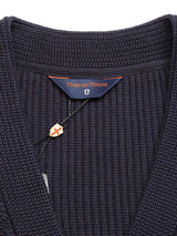 A close-up of the Achille Cardigan - Navy by Blue de Gênes shows its V-neck knit cotton design with a small decorative shield tag. Advanced knitting textures and Corozo buttons add elegance, with the brand label sewn inside.
