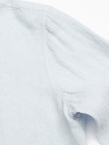 Close-up of the Enrico Beach Shirt - Blue Water by Blue de Gênes: a light blue, long-sleeve shirt highlighting shoulder and upper arm details. Soft, textured linen fabric with visible seam stitching and Corozo nut buttons. Set against a plain white background.