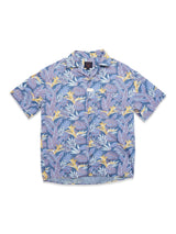 The Blue de Gênes Resort Melfi Shirt - Multi Pattern is a short-sleeved button-up made from soft denim cotton, showcasing a vivid tropical leaf and bird-of-paradise design in purple, yellow, and blue on a crisp white background.
