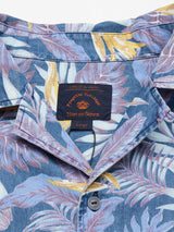 Close-up of the Resort Melfi Shirt - Multi Pattern by Blue de Gênes, showcasing a tropical design in blue, purple, and yellow on denim cotton. It features a collar, buttons, and inside label with a small logo. Size: Large.