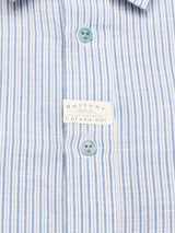 Close-up of the Enrico Grass Shirt by Blue de Gênes in a navy stripe pattern with vertical buttonholes. The buttons, featuring a subtle corozo logo, are made from natural corozo nut, accented by a small tag amid the cotton/linen fabric.
