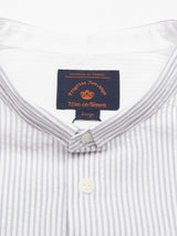 The Basso MC Shirt by Blue de Gênes is white with black yarn dye stripes, features a regular fit, two white collar buttons, and a navy label with orange text Progetto Heritage and Blue de Gênes. Made from cotton seersucker for a refined texture.