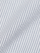 A close-up of the Basso MC Shirt - Navy Stripe by Blue de Gênes reveals a lightweight, textured cotton seersucker fabric with thin blue yarn dye stripes on a white background, creating a subtle wave pattern.