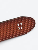 The FlexCord Belt - Cognac by Blue de Gênes is a meticulously crafted full-grain leather accessory with horizontal grooves and a small shield emblem featuring a red cross. Handmade in Italy, it rests elegantly on a plain white background.