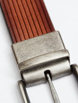 Close-up of a FlexCord Belt - Cognac by Blue de Gênes: handmade in Italy with brown full-grain leather featuring vertical grooves. The Magikflex buckles brushed metal finish beautifully contrasts the textured leather against a plain white background.