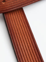 Close-up of two intersecting FlexCord Belt straps in cognac with parallel grooves, against a light surface, highlighting the detailed craftsmanship of the full-grain leather. Luxuriously handmade in Italy by Blue de Gênes.