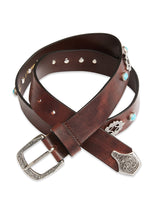 The Western Studded Belt by Blue de Gênes is crafted in Italy from dark brown full-grain leather. It features a coiled design with a silver buckle, intricate patterns, and is adorned with turquoise studs and decorative silver accents.