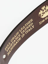 Close-up of the Blue de Gênes Western Studded Belt in Dark Brown featuring a gold embossed text FULL GRAIN LEATHER VEGETABLE TANNED HANDMADE IN ITALY, highlighted with turquoise studs and a decorative crest logo.