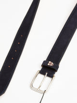 The Suede Belt - Navy by Blue de Gênes is handmade in Italy from navy blue suede leather. It features a silver buckle, multiple adjustment holes, and a small emblem near the buckle loop, laid flat on a white surface.