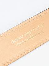 Close-up of a navy suede belt by Blue de Gênes with visible intricate stitching along the edges, highlighting its exquisite handmade craftsmanship. The belt features a beige Italian leather strap embossed in gold with the text Genuine Italian Leather Handcrafted in Italy.