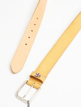 A Suede Belt - Yellow Grain by Blue de Gênes is laid flat on a light-colored surface. Its handmade in Italy, featuring a silver buckle, multiple adjustment holes, and a small cross emblem near the buckle, all with a smooth finish.