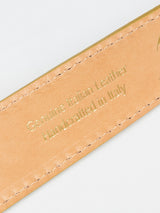 A close-up of the Blue de Gênes Suede Belt - Yellow Grain shows gold-embossed text: Genuine Italian Leather Handmade in Italy, with visible stitching on the edges, set against a light background.