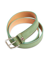 The Suede Belt - Green Bay by Blue de Gênes is a rolled-up light green suede leather belt with beige stitching, a square metal buckle, and a small cross emblem. Handmade in Italy, it features vegetable tanned tan leather on the inside.