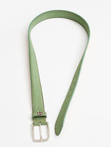 Displayed on a white background, the Suede Belt - Green Bay by Blue de Gênes features white stitching and a silver rectangular buckle. Handmade in Italy, it is crafted from green vegetable tanned leather and is coiled with the buckle end near the open loop.