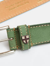 Close-up of the Green Bay suede belt by Blue de Gênes, featuring a silver buckle and small shield emblem. The green suede with tan stitching and vegetable-tanned leather inner side is embossed with Genuine Italian Leather, Handmade in Italy.
