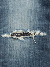 Close-up of blue denim fabric from Blue de Gênes Giacomo Osaka Jeans - Dark Denim, featuring a relaxed loose fit and a central horizontal rip exposing frayed white threads and a dark area beneath.