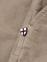 A small white shield pin with a red cross accents the pocket seam of the tan BGpaulo Ottawa Trousers - Fungi by Blue de Gênes, adding a subtle touch to these classic Italian-made chinos.