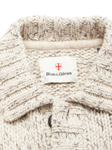 Close-up of the Sakura Knit Cardigan - Stone by Blue de Gênes, a chunky beige wool blend cardigan with a collar and a white label featuring the brand name and red cross emblem—ideal for layering on cooler days.