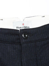 Close-up of the waistband of the Blue de Gênes Kibishi Solid Pant in dark navy, made from an Italian wool blend, with a black button and a white Blue de Gênes label beneath a small red and white shield emblem.