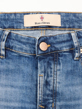 Close-up of the waistband and front button of Vinci Girisha Used Jeans by Blue de Gênes, made from comfort stretch denim. The button has a crest design, and an inner label reads Blue de Gênes beneath a red and white shield emblem.