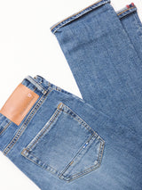 Blue de Gênes Vinci Girisha Used Jeans in blue comfort stretch denim are laid flat on a white background, highlighting the back pocket and a tan branded leather patch on the waistband.