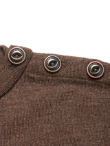 Close-up of the Toyama Knit L/S - Brown by Blue de Gênes, a Merino wool sweater featuring three black buttons with thin red borders and engraved text along the shoulder seam.