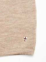 Close-up of the Blue de Gênes Toyama Knit L/S in oat, featuring textured beige Merino wool and a small shield patch near the edge with a maroon cross on a white background.