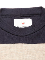 Close-up of the Blue de Gênes Toyama Stripe Knit L/S in dark navy, featuring a crewneck with a white label inside the collar showing a red shield emblem, Blue de Gênes text, and a stylish beige panel below the collar.