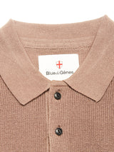 Close-up of the textured, light brown Porto Polo Knit - Fungi shirt by Blue de Gênes, featuring two black buttons and a collar label with the brand name and red cross emblem—a wool polo that exudes casual elegance.