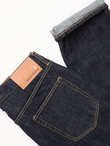 The Marco Rinse Jeans - Rinse Wash by Blue de Gênes are dark blue, relaxed-fit denim jeans with yellow stitching and a brown leather waistband patch; one cuff reveals the 100% cotton inner fabric.