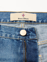 Close-up of Blue de Gênes Marco Used Jeans - Used, made from 100% cotton denim, showing the waistband, embossed logo button, partly open zipper, and tan label with red and white shield emblem. Made in Greece.