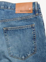 Close-up of the back pocket and waistband of Marco Used Jeans - Used by Blue de Gênes, made in Greece from blue 100% cotton denim. Features a brown leather brand patch with shield logo, visible stitching, and a faded, worn finish.