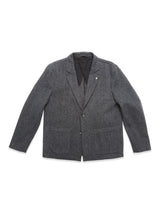 The Blue de Gênes Fukui Blazer - Black Pattern is a dark gray wool herringbone blazer with relaxed tailoring, notched lapel, two front pockets, and a chest pocket, shown laid flat on a white background.
