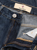 Close-up of blue BGmarco Rowan Jeans - Used by Blue de Gênes, showing a partially open zipper and button. The relaxed fit jeans display an inner label with the Blue de Gênes name and a small cross emblem above it.