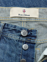 Close-up of Blue de Gênes BGgiacomo Tim Jeans in antique wash, featuring metal shield-logo buttons, a cream Blue de Gênes label, and a red-white shield emblem above the waistband. Made in Italy from premium denim.