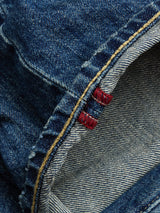 Close-up of BGgiacomo Tim Jeans - Antique wash by Blue de Gênes, showing blue rigid denim with a folded edge, yellow stitching, red embroidered tags, and clearly visible texture and weave.