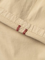 Close-up of pale khaki corduroy fabric from the Blue de Gênes BGmenzo Vecchio Chino, featuring a visible seam and two red stitched bar tacks that highlight its vintage-inspired design.