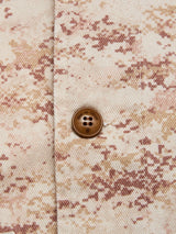 Close-up of the BGkendrick Print Jacket - Multi Pattern by Blue de Gênes, featuring beige and brown camo cotton twill fabric with a brown four-hole button, highlighting texture and stitching details.