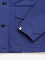 Close-up of the BGcanopy Jacket - Navy Peony by Blue de Gênes, featuring sturdy heavy cotton, front pocket, sleeves, black buttons, and a rectangular tag with a red and blue logo near the cuff—reflecting its workwear heritage and structured design.