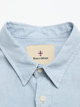 Close-up of the collar and top buttons of the BGenric Hope L/S Shirt - Blue Fog by Blue de Gênes. A beige tag with a red and white shield logo highlights this refined, breathable summer shirt’s stylish details.