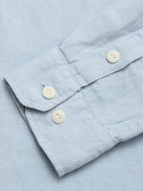 A close-up of the Blue de Gênes BGenric Hope L/S Shirt in Blue Fog shows its light blue linen sleeve with two white cuff buttons and visible seam detail, lying flat on matching fabric—an ideal breathable summer shirt.