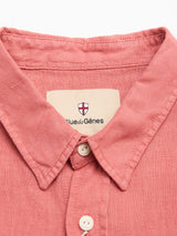Close-up of the BGenric Hope L/S Shirt in Coral by Blue de Gênes—a pink breathable linen summer shirt with a pointed collar, white buttons, and an inner label featuring the brand name under a small shield logo.